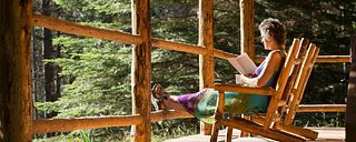 A woman reads by sunlight on the porch of a cabin at Minam River Lodge