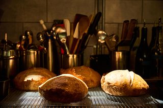 Freshly baked loaves of bread cool on a wire rack in a warmly lit kitchen, with utensils and bottles in the background.